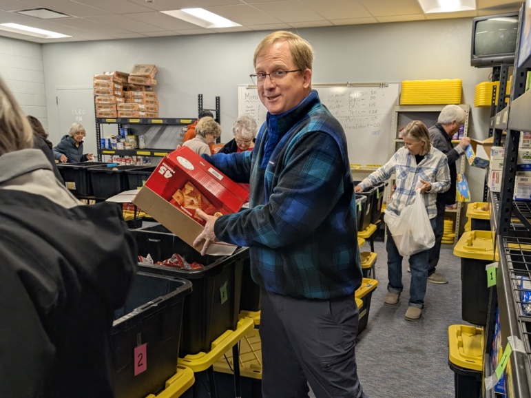 A man empties a box of snacks into a rural Arizona school food pantry container