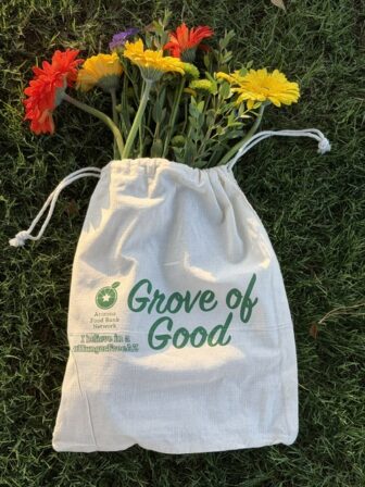 Grove of Good branded produce bag laying in the grass with flowers peeking out of the bag.